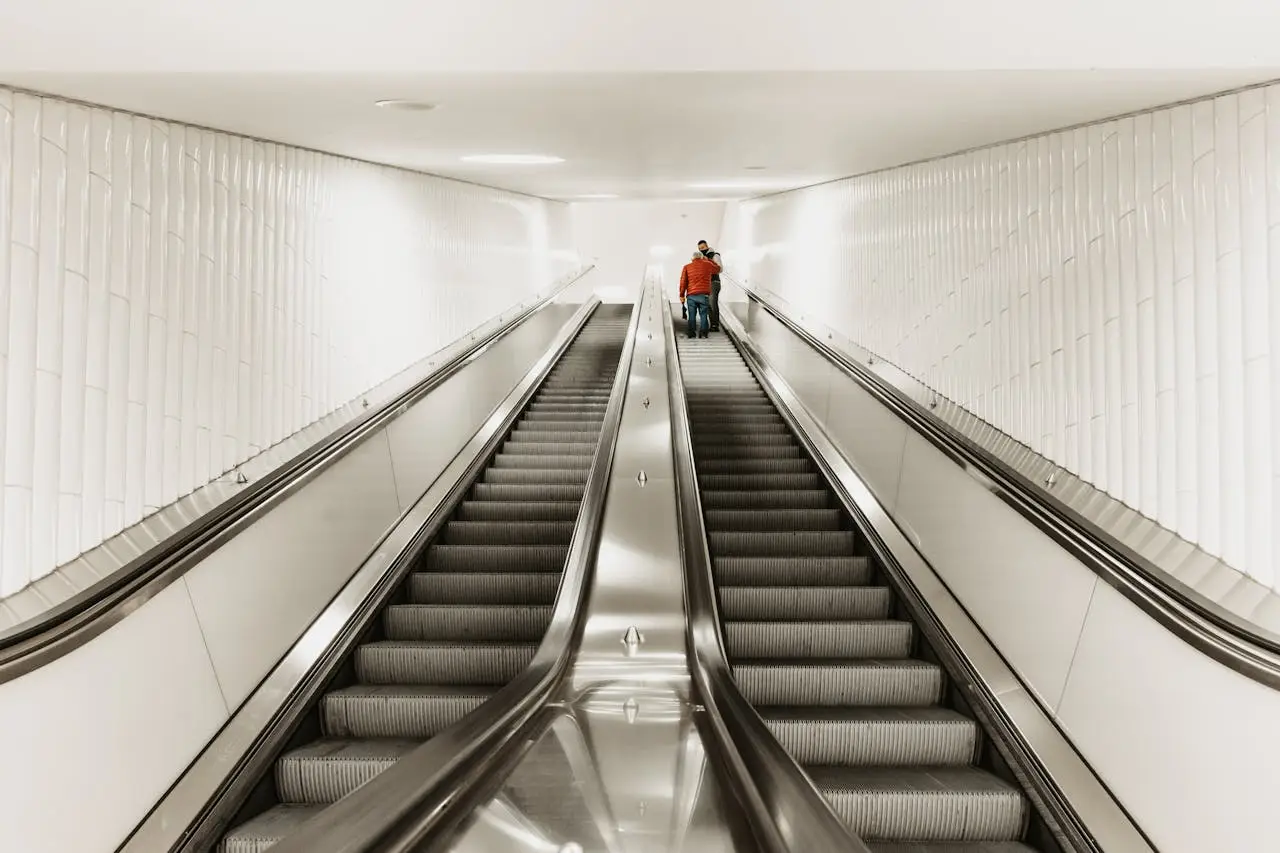 A modern urban subway station featuring illuminated escalators leading to a platform.