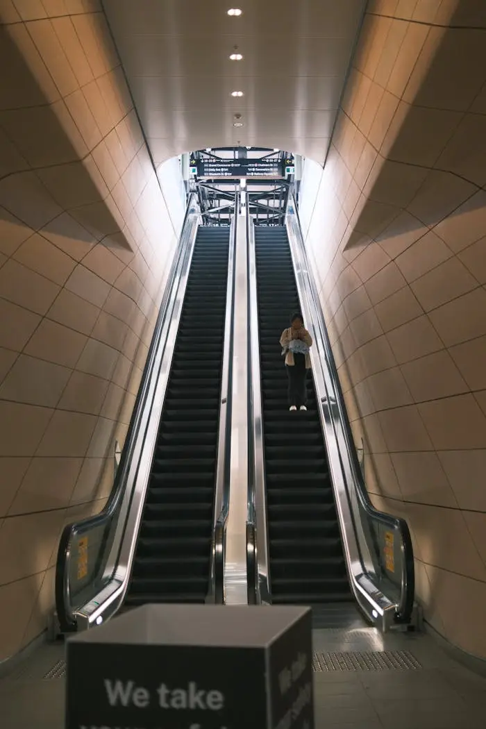 A lone person ascends an escalator in a sleek, modern subway station.