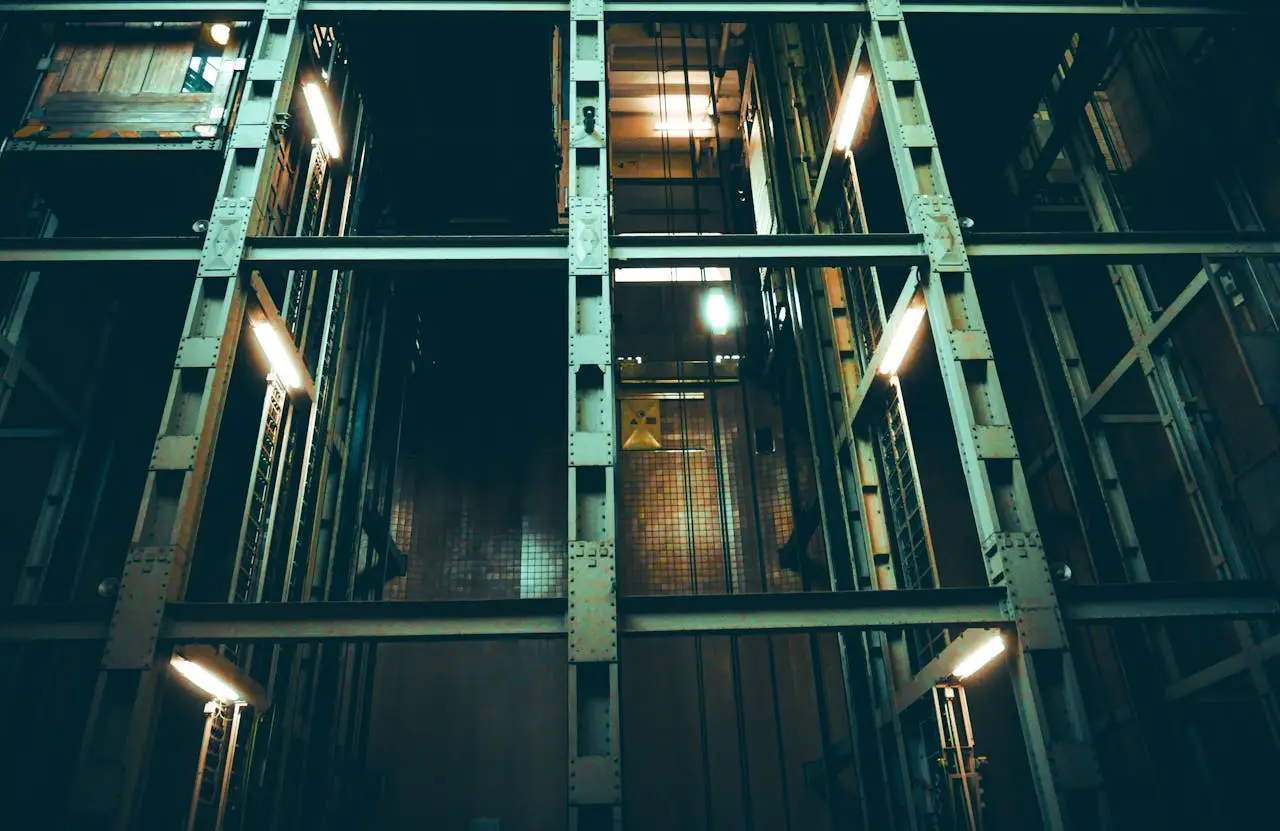 A dimly lit industrial elevator shaft with metal framework and lights.